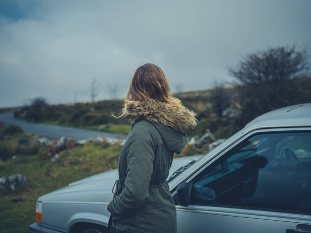 A young woman is standing by her car on the moor in the autum - Фото, изображение