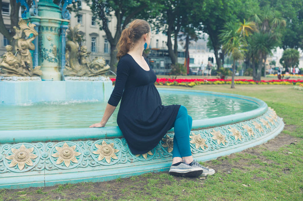 A young woman is sitting by a fountain in the park - Foto, immagini