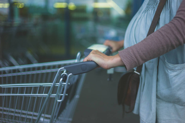 Uma jovem grávida está empurrando um carrinho de compras fora de um supermercado
 - Foto, Imagem