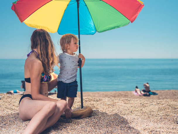 Egy fiatal anya és a kisgyermek a pihentető alatt egy napernyő a strandon - Fotó, kép