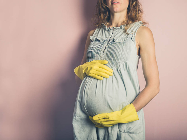 A young pregnant woman is wearing yellow rubber gloves - Valokuva, kuva