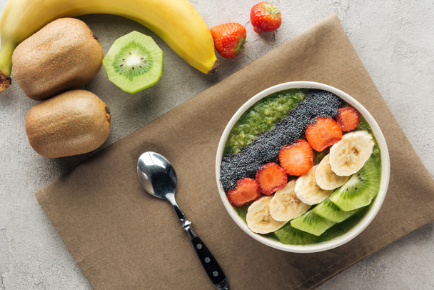 top view of smoothie bowl with fresh fruits, spoon and ingredients on grey background - Foto, Imagem