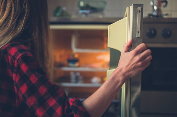 A young woman is opening the door of her fridge - Valokuva, kuva