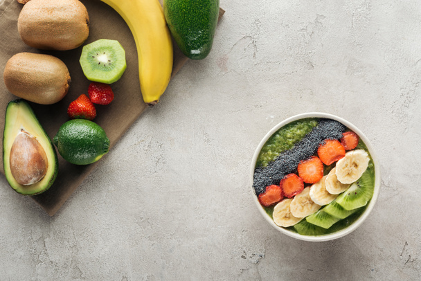 top view of smoothie bowl with fresh fruits and ingredients on grey background with copy space - Foto, immagini