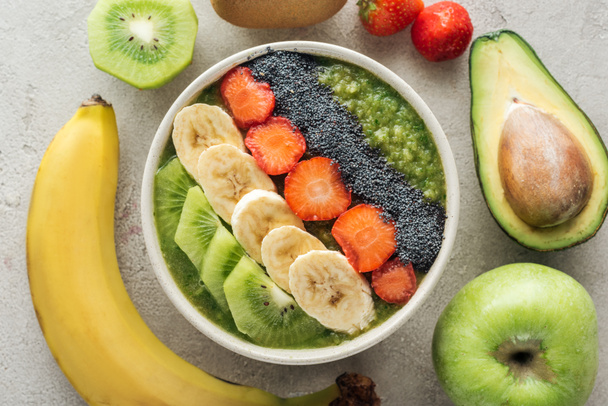 top view of delicious smoothie bowl with fresh fruits and ingredients on grey background - Photo, Image