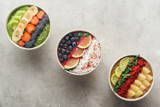 vista superior de tazones de batido orgánicos saludables con frutas sobre fondo gris
 - Foto, Imagen