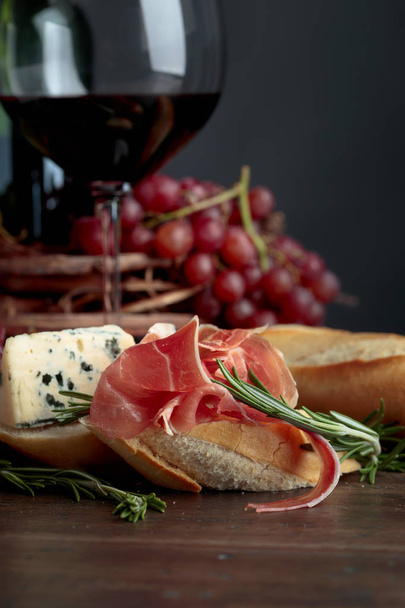 Sandwich with prosciutto, blue cheese and rosemary on a dark background. Delicious snack and red wine. Copy space for your text. - Zdjęcie, obraz