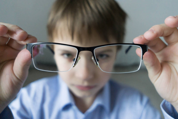 a 9-year-old boy in a blue shirt with glasses checks his eyesight. Dissatisfied with the fact that prescribed glasses - does not want to wear. Eye health care. - Photo, image