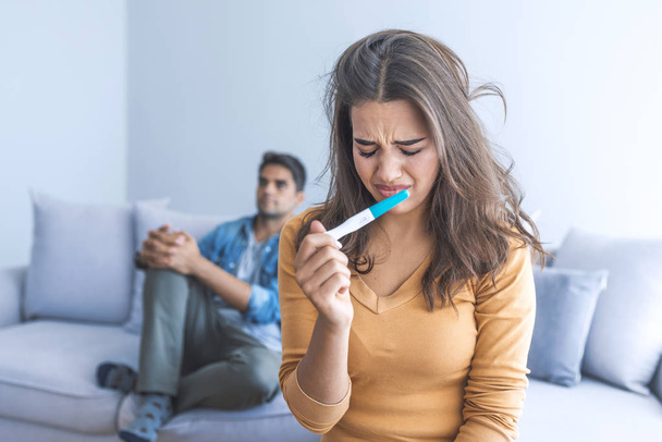 Upset woman holding pregnancy test with man at background - Zdjęcie, obraz