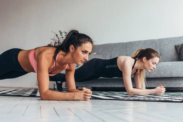 Dwie kobiety fit robi ćwiczenia deski, na piętrze w domu szkolenia powrót i naciśnij, mięśnie, trening fitness, sport - Zdjęcie, obraz