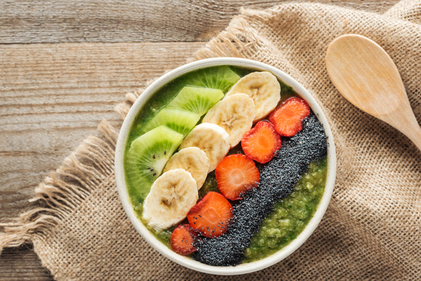 top view of fresh smoothie bowl on sackcloth and wooden background - Foto, Imagem