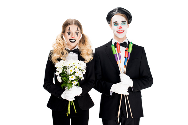 cheerful couple of clowns holding flowers and firecrackers in hands isolated on white  - Photo, Image