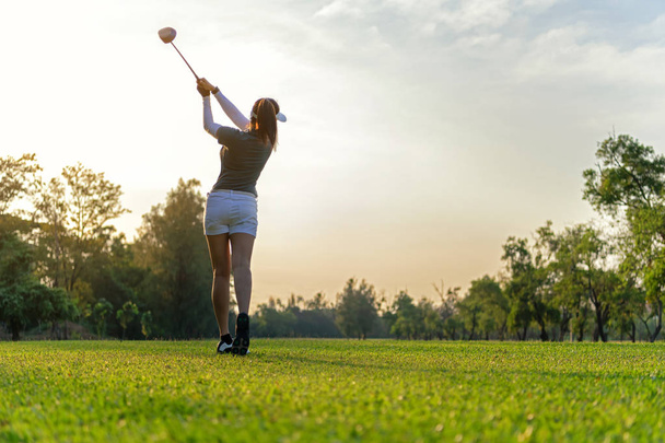 Sport Healthy. Asian sporty woman golf player doing golf swing tee off on the green sunset evening time, she presumably does exercise. Healthy and Lifestyle Concept. - Fotoğraf, Görsel