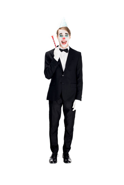 cheerful clown in suit and birthday cap holding blower isolated on white  - Photo, Image