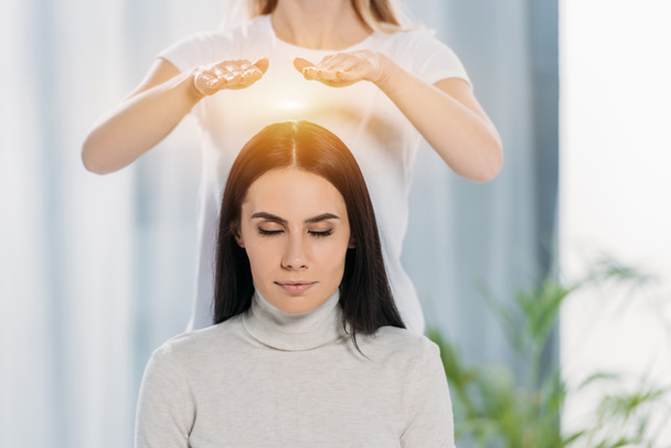 peaceful young woman with closed eyes receiving reiki healing therapy above head  - Foto, imagen