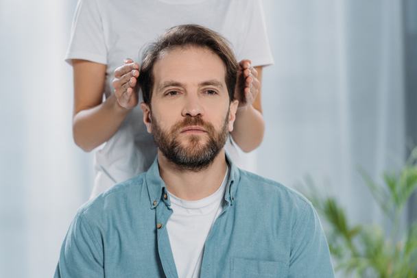 Oříznout záběr vousatý muž sedí a přijímající reiki ošetření na hlavě - Fotografie, Obrázek