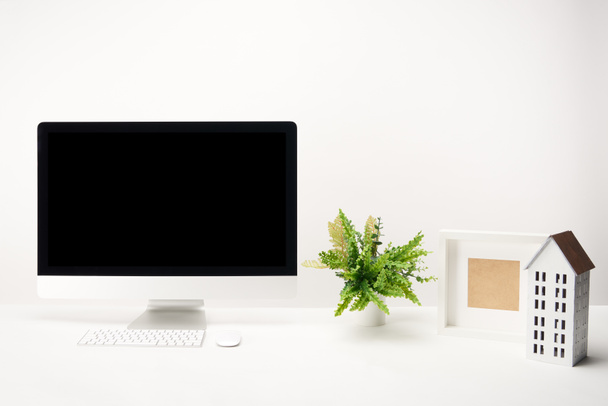 workplace with plant, house model, photo frame and desktop computer with copy space isolated on white - Foto, afbeelding
