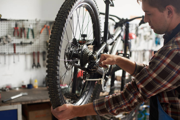 male mechanic working in bicycle repair shop, repairman fixing bike using special tool, wearing protective work wear - Foto, immagini