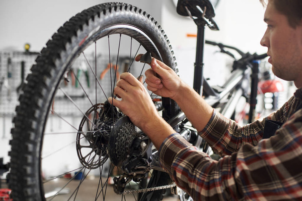 male mechanic working in bicycle repair shop, repairman fixing bike using special tool, wearing protective work wear - Foto, Imagem