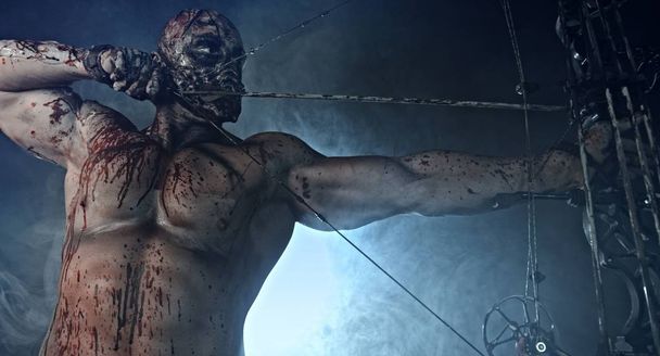portrait of bloody zombie killer with modern bow aiming against misty dark background - Фото, зображення