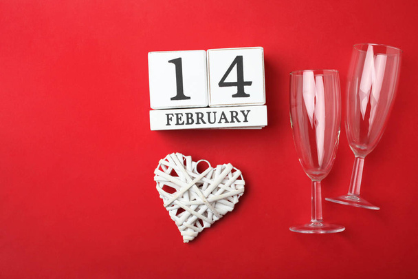 Calendário de madeira com data 14 de fevereiro, coração branco e copo de champanhe em fundo vermelho brilhante. Encontro romântico. Conceito Dia dos Namorados
. - Foto, Imagem