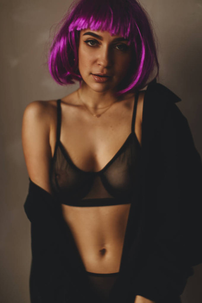 Ελκυστική κοπέλα φορούν ροζ περούκα και μαύρα εσώρουχα, πουκάμισο. Γυναίκες κλείνουν ένα μαύρο πουκάμισο. Σέξι κορίτσι απογειώνεται ή βάζοντας μαύρο πουκάμισο.  - Φωτογραφία, εικόνα