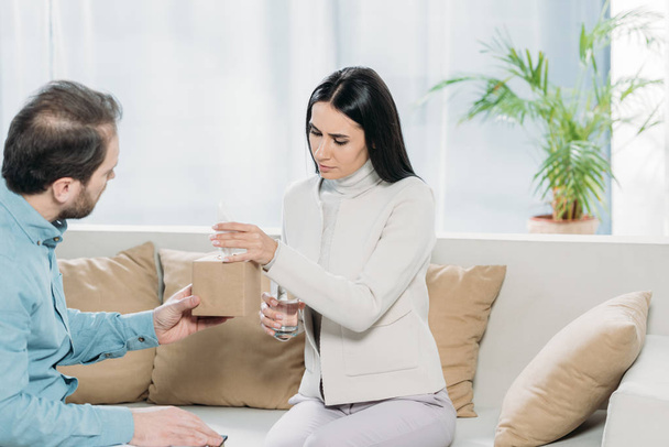 psychotherapist with clipboard giving paper tissues to upset young patient with glass of water  - Photo, Image