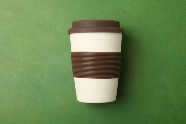 Une tasse en plastique beige jetable avec du silicone brun sur fond vert. Vue du dessus, espace de copie
. - Photo, image