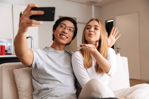 alegre joven pareja tomando un selfie mientras sentado en un sofá en casa
 - Foto, imagen