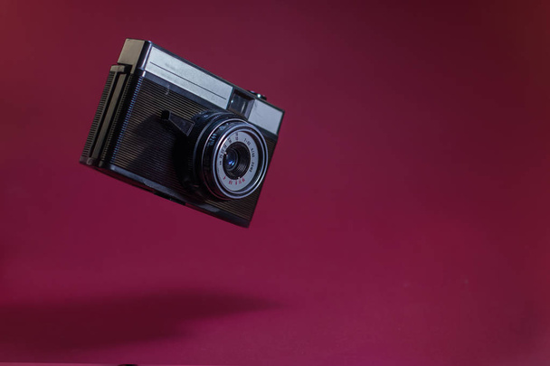 Old retro camera on red background flying in air. - Photo, Image