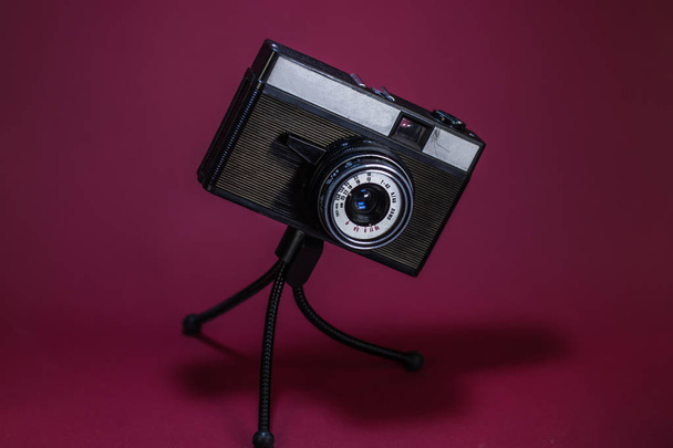 Стара ретро камера на червоному тлі на тринозі
. - Фото, зображення