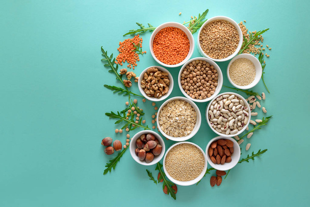 Set of bowls with organic quinoa, lentil, chickpea, wheat, walnut, almond, hazelnut and sesame. Cereals and legumes assortment on blue paper background. Top view. Copy space. Flat lay - Фото, изображение