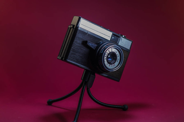 Старая ретро камера на красном фоне на штативе
. - Фото, изображение