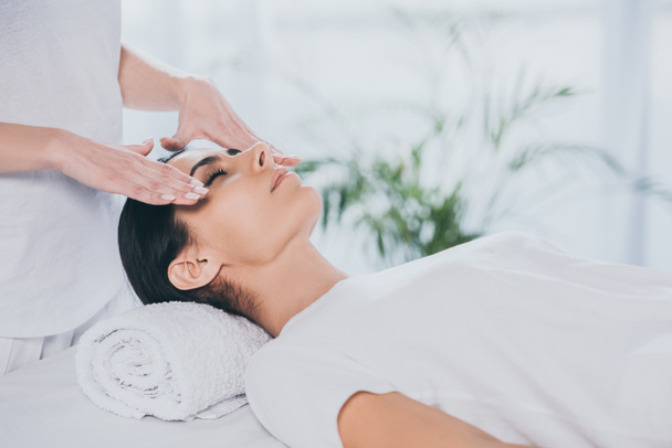 cropped shot of young woman with closed eyes receiving reiki treatment on face - Photo, Image