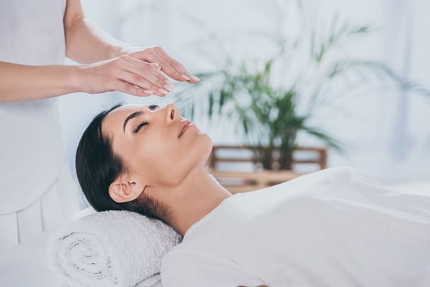 cropped shot of calm young woman with closed eyes receiving reiki treatment above head - Photo, Image