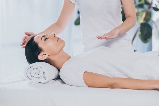 peaceful young woman receiving reiki healing treatment on head and chest - Photo, Image