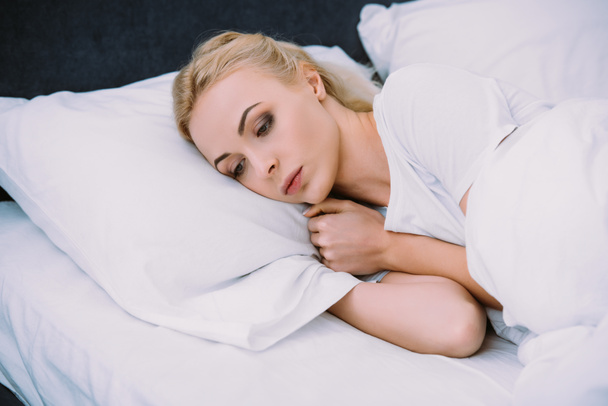 bela mulher triste segurando cobertor enquanto deitado na cama em casa
 - Foto, Imagem