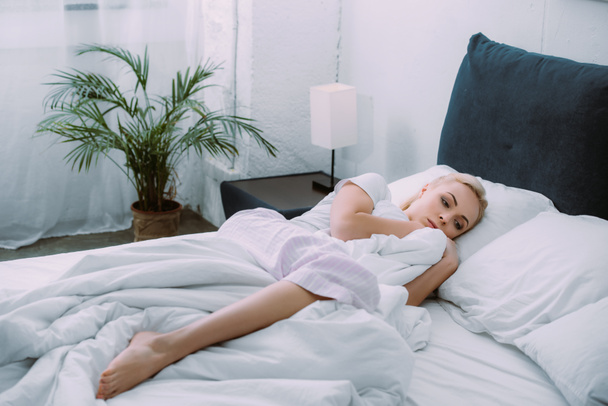mujer triste sosteniendo la manta mientras está acostado en la cama en casa
 - Foto, Imagen