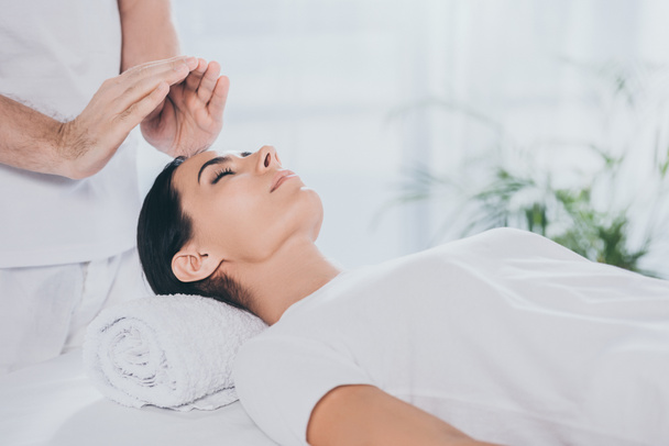 cropped shot of calm young woman with closed eyes receiving reiki therapy  - Foto, afbeelding