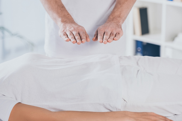 cropped shot of woman receiving reiki healing session above stomach - Zdjęcie, obraz