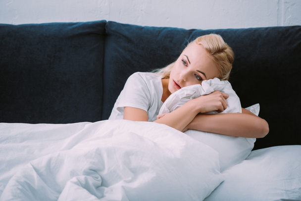 αναστατωμένος γυναίκα κρατώντας κουβέρτα στο κρεβάτι στο σπίτι και βλέπει μακριά - Φωτογραφία, εικόνα