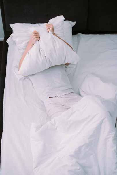 donna depressa che copre il viso con un cuscino mentre si trova a letto a casa
 - Foto, immagini