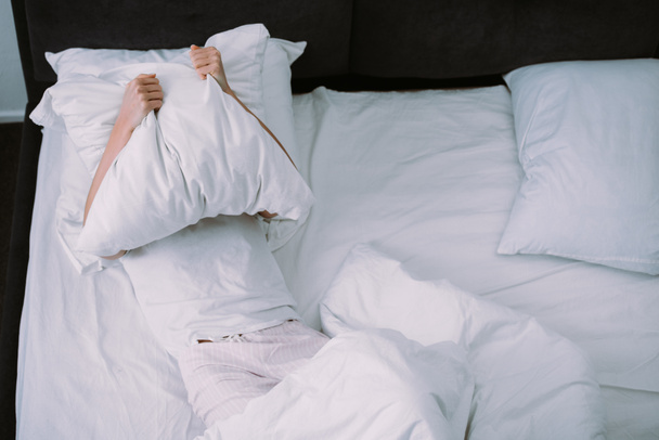 подавленная женщина покрывает лицо подушкой, лежа в постели дома
 - Фото, изображение