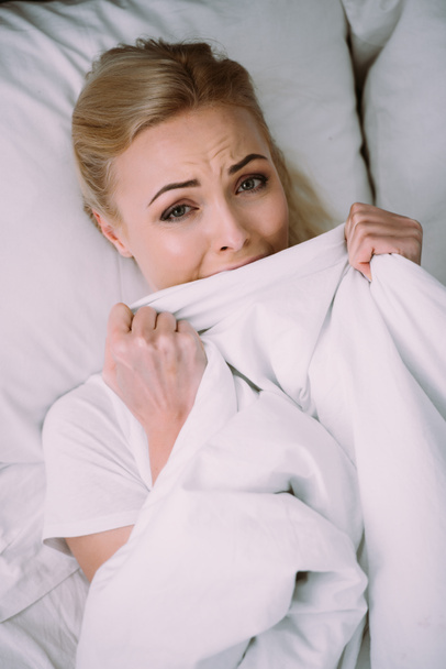 frightened woman lying in bed, crying and holding blanket  - Foto, imagen