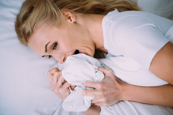 vyděšená žena leží, brečí a drží deku v posteli doma - Fotografie, Obrázek