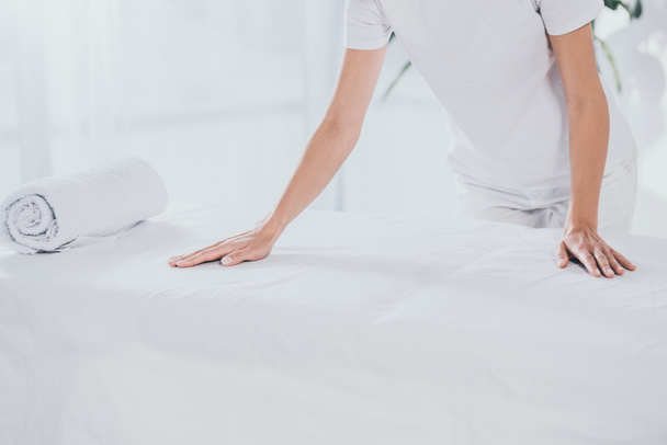abgeschnittene Aufnahme eines medizinischen Mitarbeiters, der sich mit gerolltem Handtuch an einen weißen Massagetisch lehnt - Foto, Bild