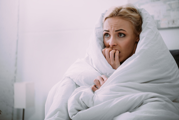 selective focus of scared woman covered in blanket biting hand in bed  - Photo, Image