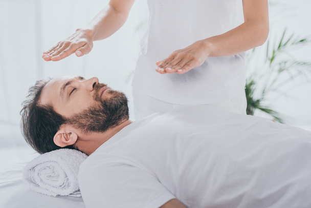 cropped shot of healer doing reiki healing session to calm bearded man with closed eyes - Photo, Image