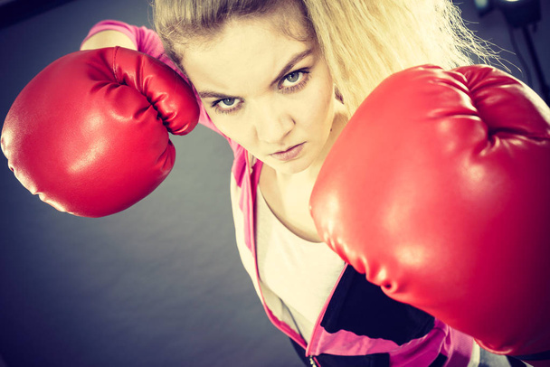 Sporty angry determined woman wearing red boxing gloves, fighting. Studio shot on dark background. - Фото, изображение