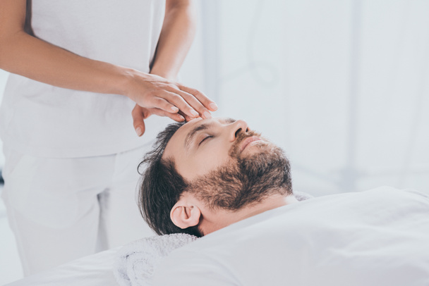 calm bearded man with closed eyes receiving reiki healing therapy on head - Foto, imagen